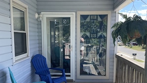 A covered porch with two chairs, a patterned rug, and a view through glass doors. - Beach, Please! (Kill Devil Hills)