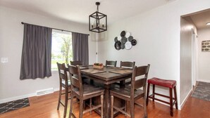 Un coin repas avec une table et des chaises en bois, un luminaire suspendu et une composition décorative de plaques murales.