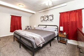 A bedroom with a bed, a nightstand, a dresser, a ceiling fan, and a wall art piece.