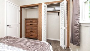 Une chambre à coucher comprenant un lit, une commode en bois et un dressing avec des portes coulissantes.