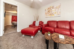 A living room with a red leather sofa, a matching ottoman, and two small wooden tables.