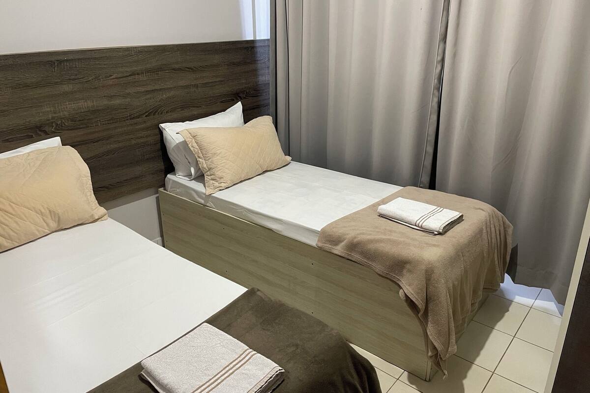Une chambre à coucher avec deux lits, chacun doté d’une tête de lit en bois, de draps blancs et d’oreillers beiges.