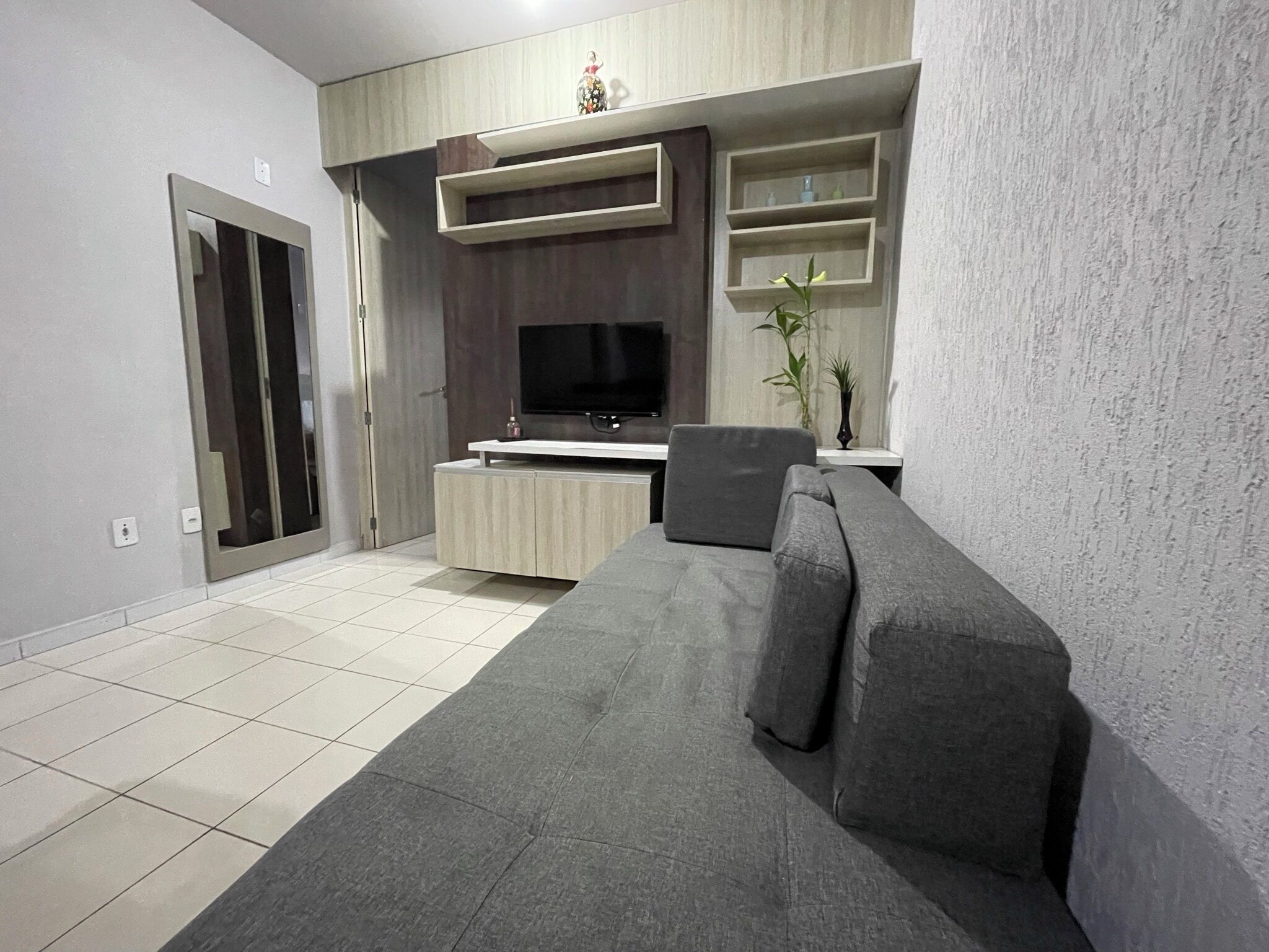 Een moderne woonkamer met een grijze bank, een flatscreen televisie en inbouwplanken.