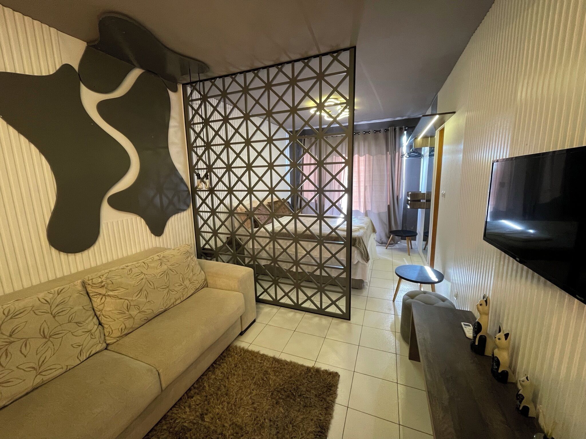 A living room with a sofa, a TV, a decorative wall, and a partition with a geometric pattern.