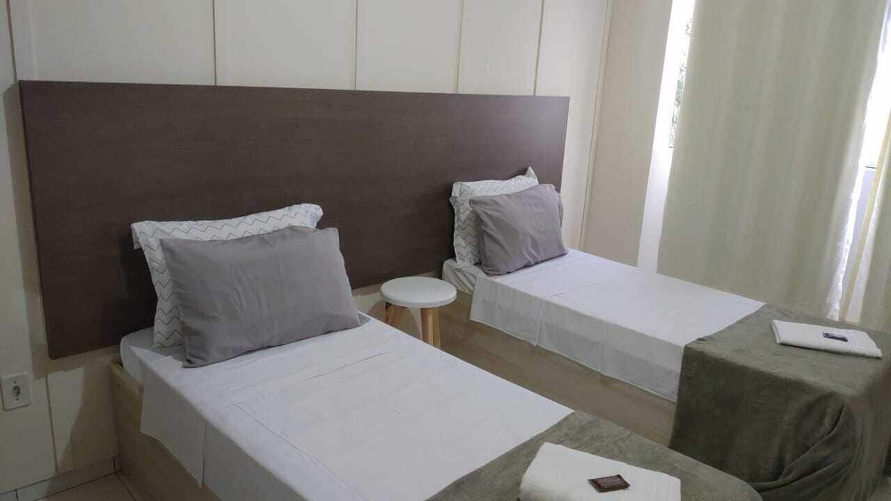 Habitación de hotel con dos camas individuales, una mesa redonda pequeña y un ordenador portátil sobre una mesita auxiliar.