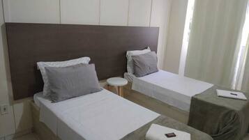 Habitación de hotel con dos camas individuales, una mesa redonda pequeña y un ordenador portátil sobre una mesita auxiliar.