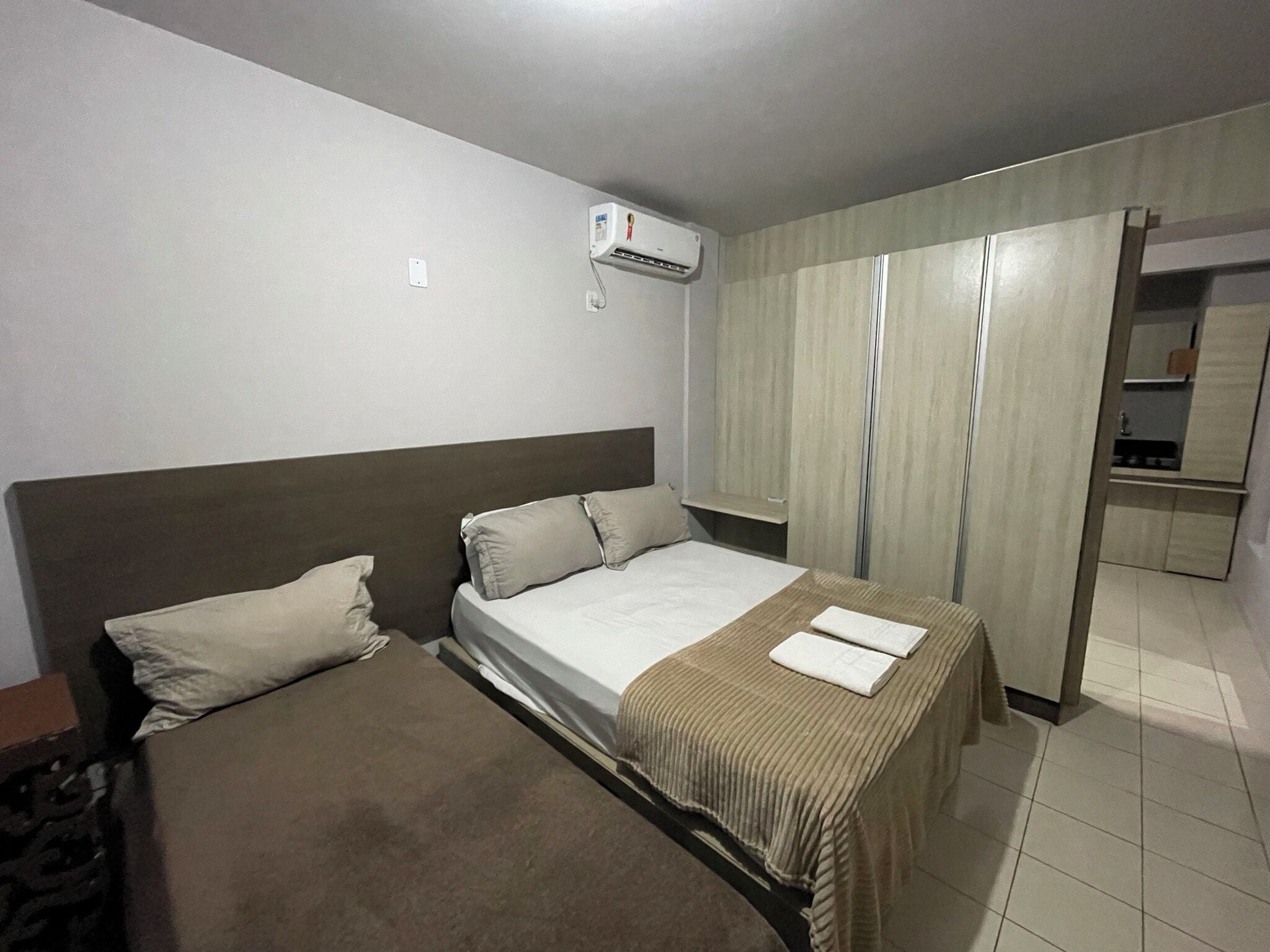 A hotel room with two beds, a wardrobe, and an air conditioning unit.