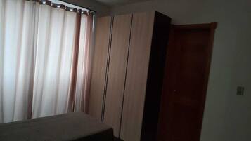Une pièce comprenant un lit, une armoire, une porte et des rideaux.