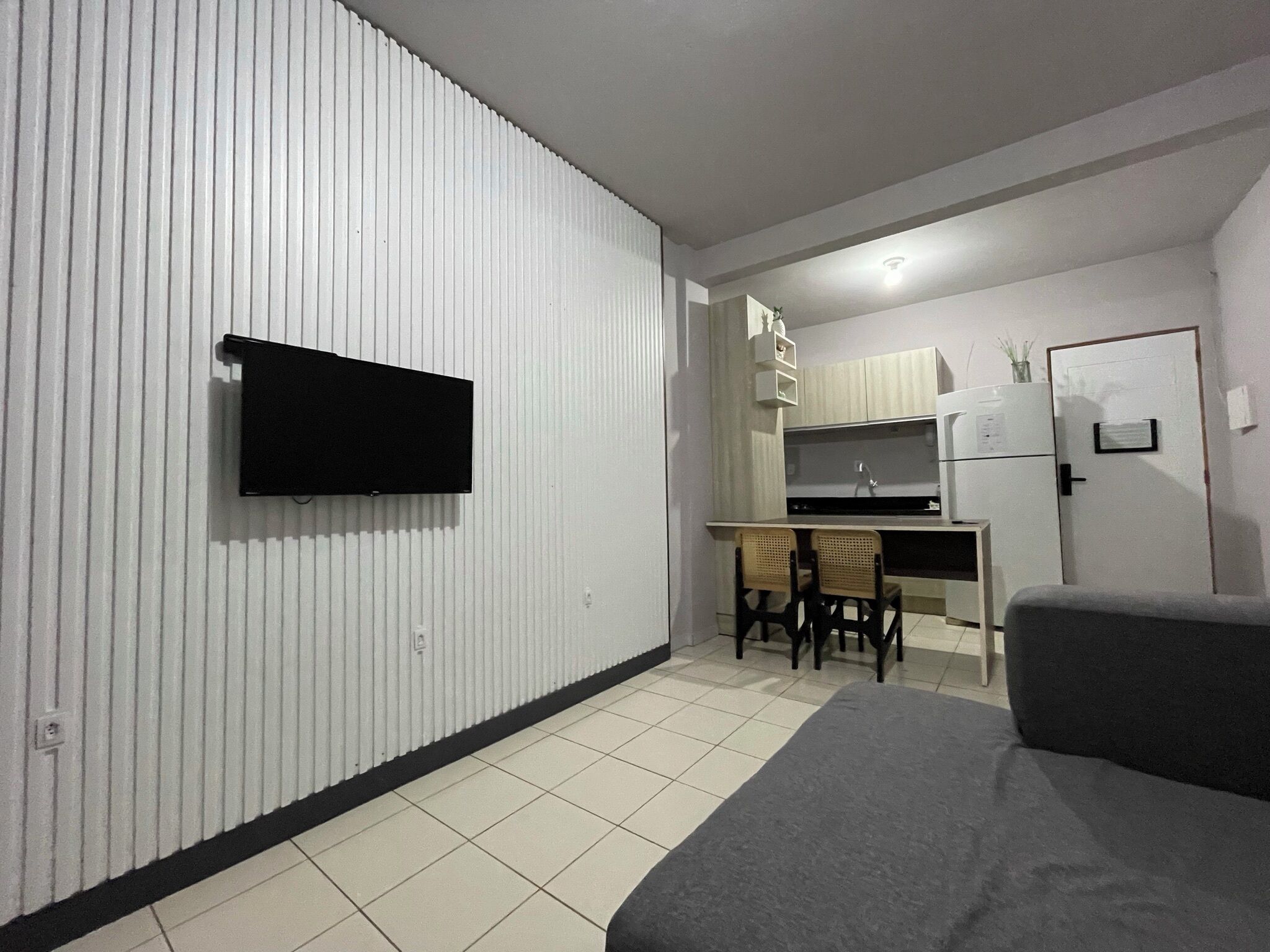 A compact living space with a kitchenette, a flat-screen TV mounted on a wall, a dining area with a table and chairs, and a sofa.