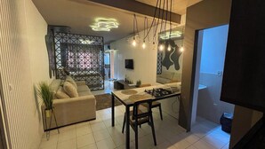 A modern living room with a sofa, a dining table, and a kitchen area.