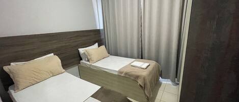 A hotel room with two beds, a wooden headboard, a grey curtain, and a tiled floor.