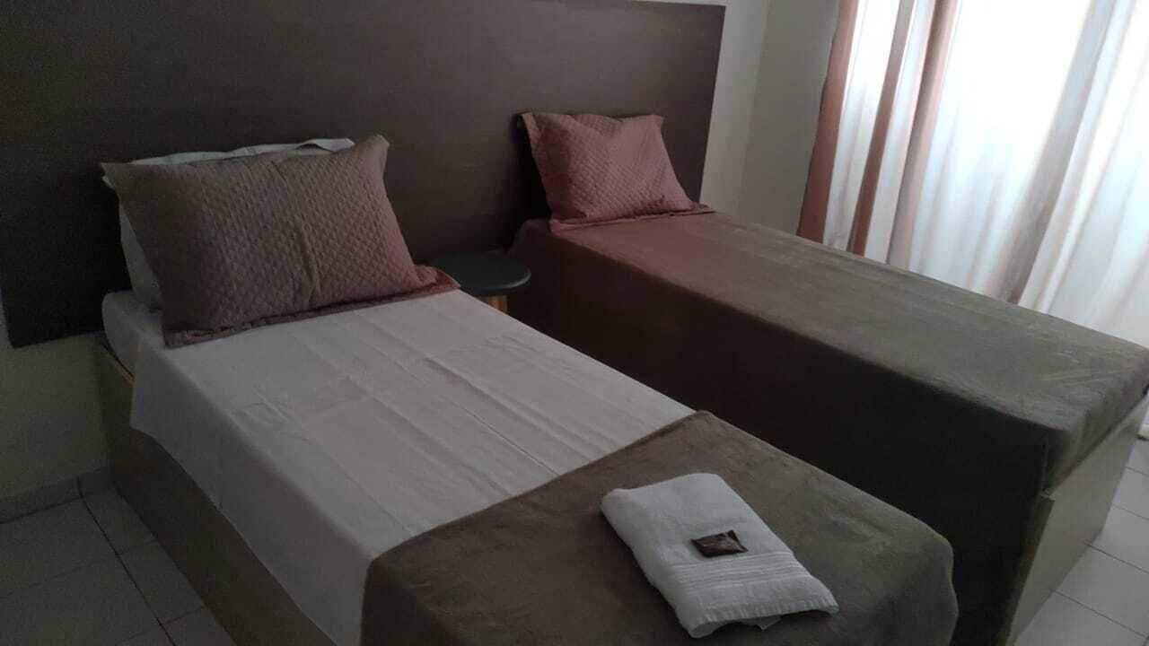 A hotel room with two single beds, a small table, and a window with curtains.