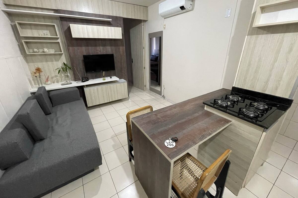 Une cuisine moderne dotée d’une cuisinière intégrée, d’une table à manger avec des chaises, d’un canapé gris et d’un téléviseur posé sur un meuble en bois.