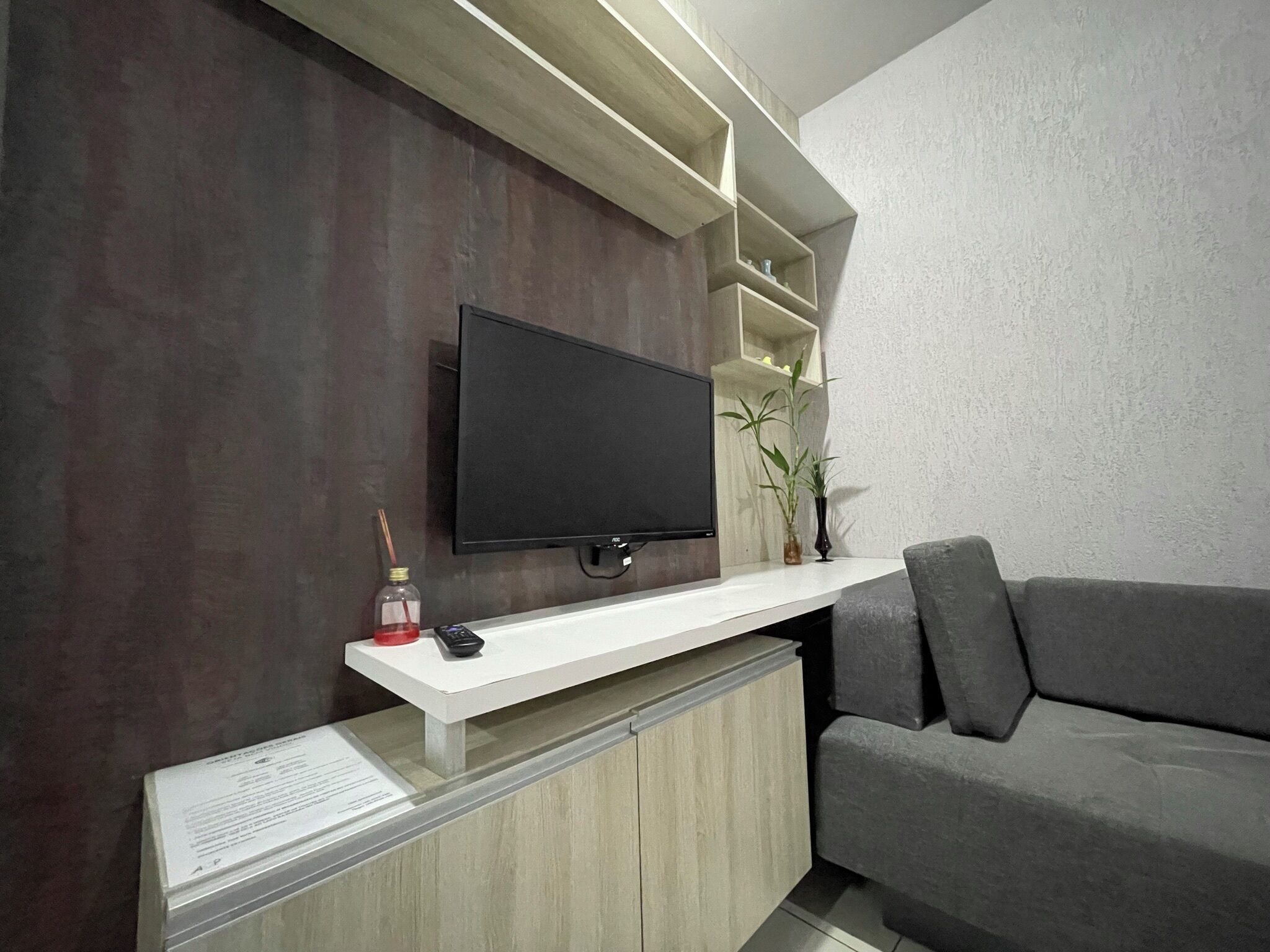 Una sala de estar moderna con un televisor de pantalla plana montado en una pared de madera, una consola blanca, un sofá gris y una pequeña planta.