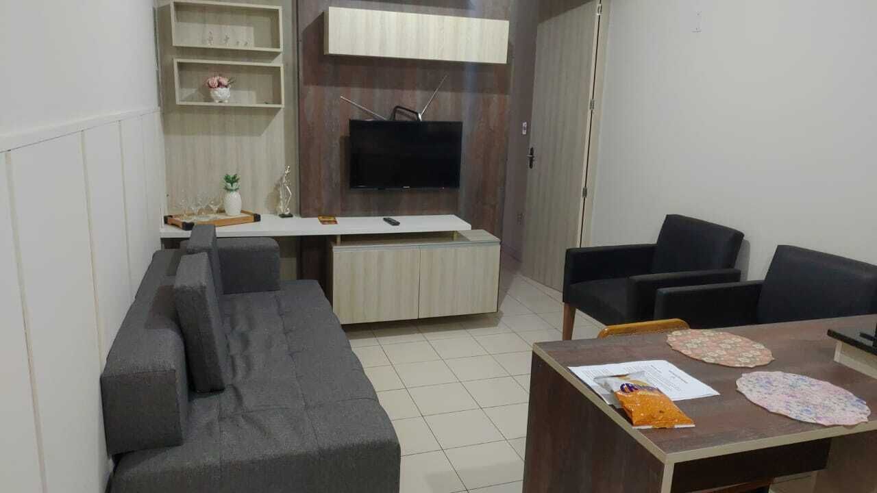 A living room with a sofa, chairs, a TV, and a small table with papers and a bag.