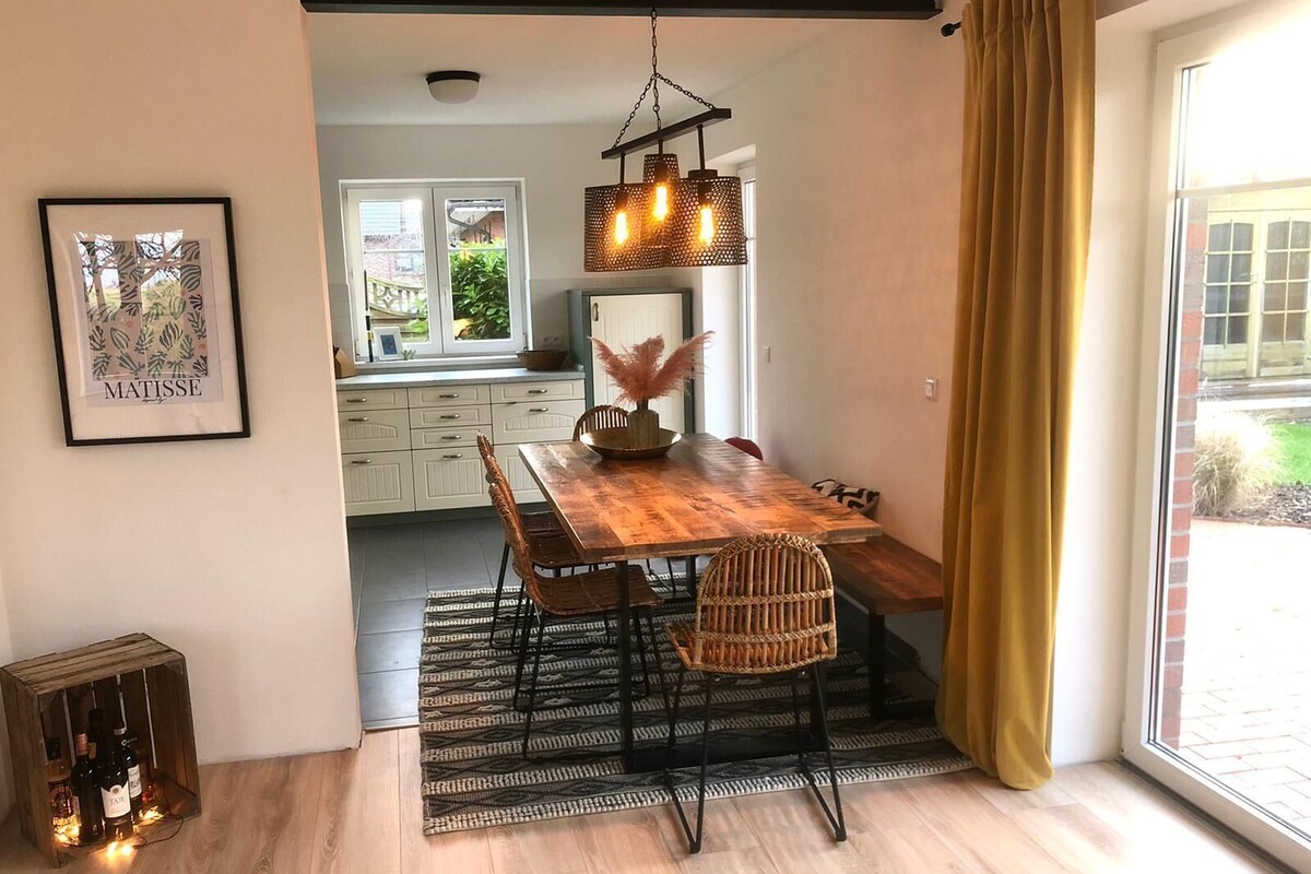 A dining area with a wooden table, wicker chairs, and a hanging light fixture.