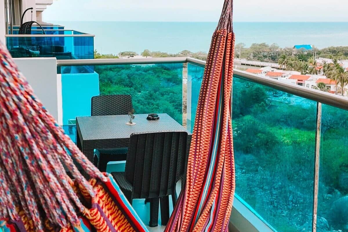Ein Balkon mit einer Hängematte, einem Tisch und Stühlen mit Blick auf eine Küstenlandschaft und freiem Blick aufs Meer.