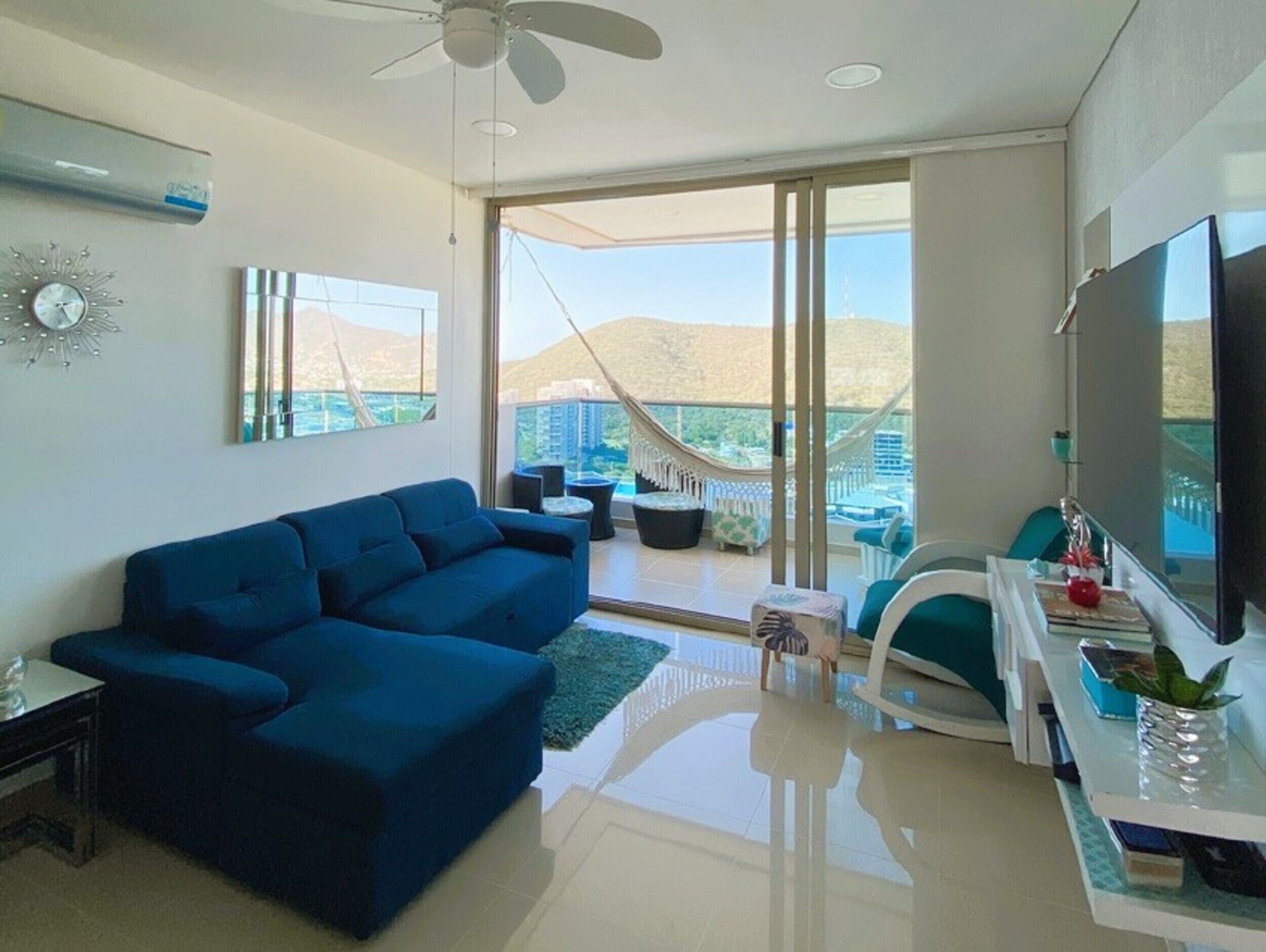 Ein modernes Wohnzimmer mit einem blauen Sofa, einem Flachbildfernseher und einem Balkon mit Blick auf die Stadt.