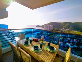 Una mesa de comedor dispuesta con platos, vasos y cubiertos en un balcón con vistas a la ciudad y al mar.