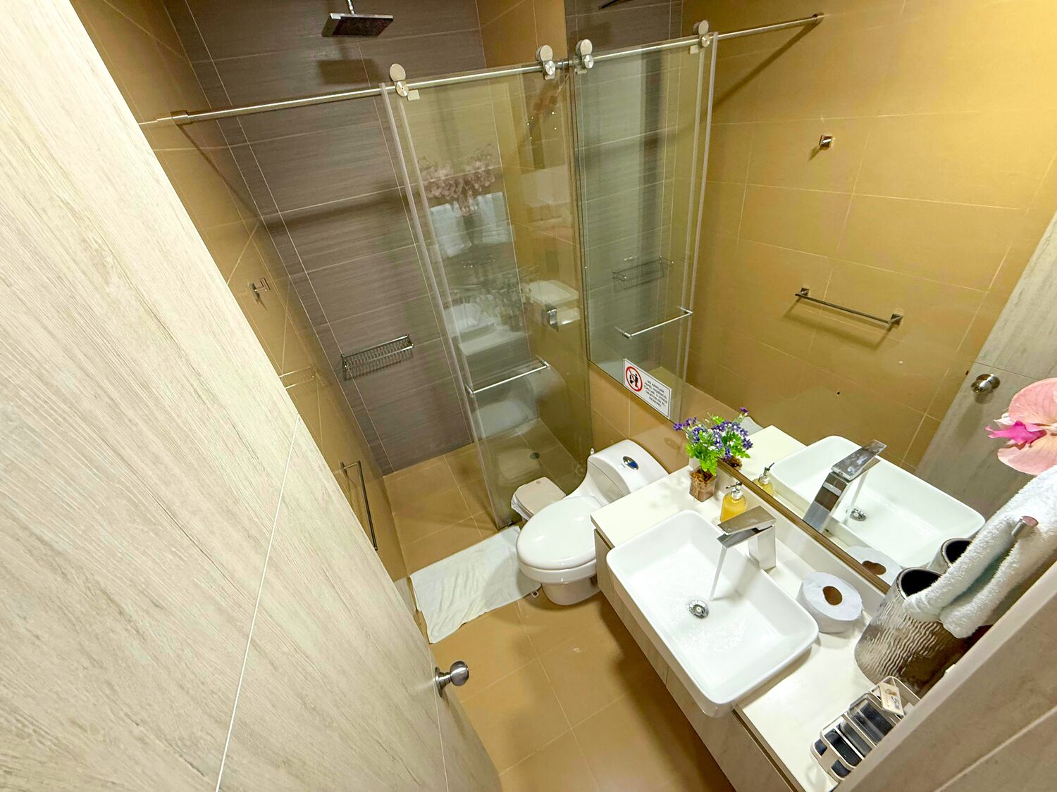 A modern bathroom with a glass-enclosed shower, a toilet, a sink, and a towel rack.