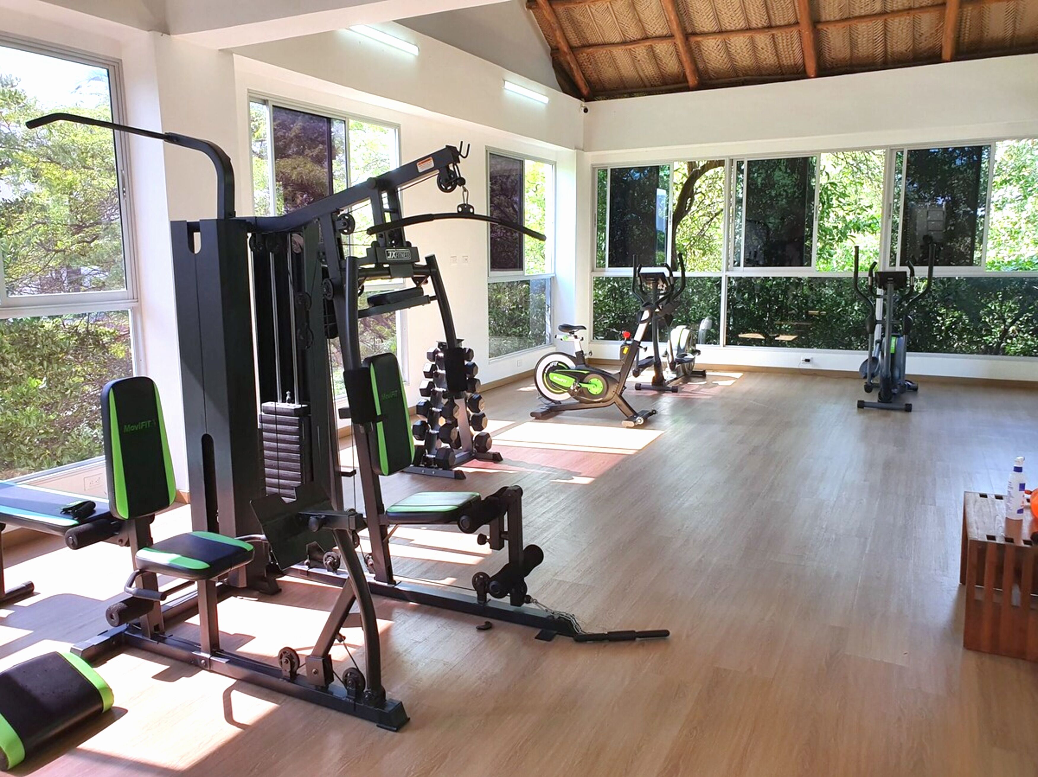 Une salle de sport équipée de divers appareils d’exercice, dotée de grandes fenêtres et d’un plancher en bois.