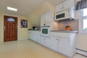 A kitchen with white cabinets, a microwave, an oven, and a window with a curtain.