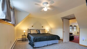 A bedroom with a bed, two bedside lamps, a ceiling fan, and a door leading to another room.
