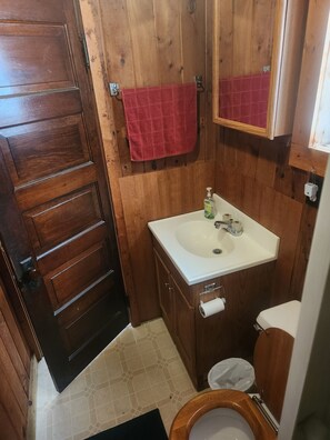 Een houten badkamer met een wit wastafelmeubel, een rode handdoek en een houten toilet.