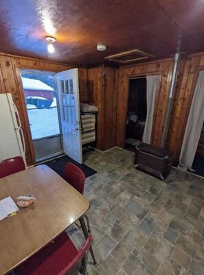 Une pièce avec un intérieur en bois, une table à manger avec des chaises, un réfrigérateur et une porte donnant sur l’extérieur.