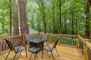 Eine Holzterrasse mit Tisch und Stühlen, umgeben von hohen Bäumen und einem Geländer.