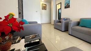 A modern living room with two grey sofas, a coffee table, and a vase with red flowers. There is a framed picture on the wall and a door in the background.