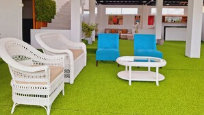 A modern indoor space with white wicker furniture, a green artificial turf floor, and a bright blue sofa.