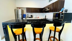 A modern kitchen with dark wooden cabinets, a black countertop, and three bar stools with yellow cushions.