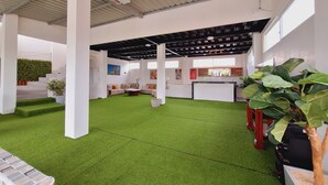 A spacious indoor area with artificial grass flooring, a seating area with sofas and a coffee table, and a bar counter with a wine rack.
