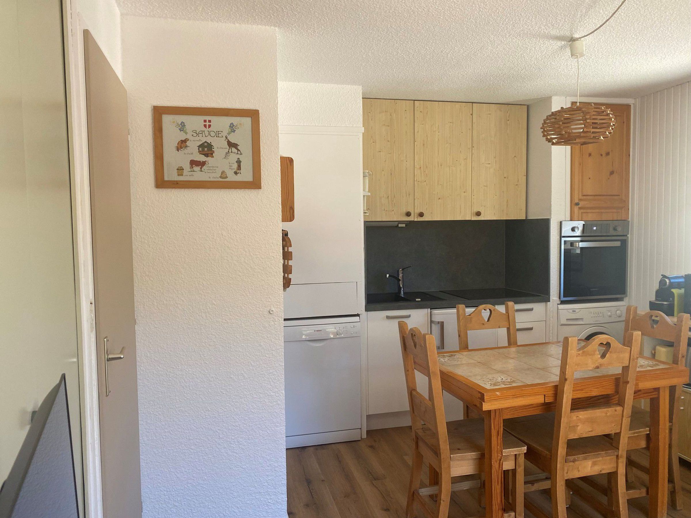 A compact kitchen with wooden cabinets, a built-in oven, and a dining area with a wooden table and chairs.