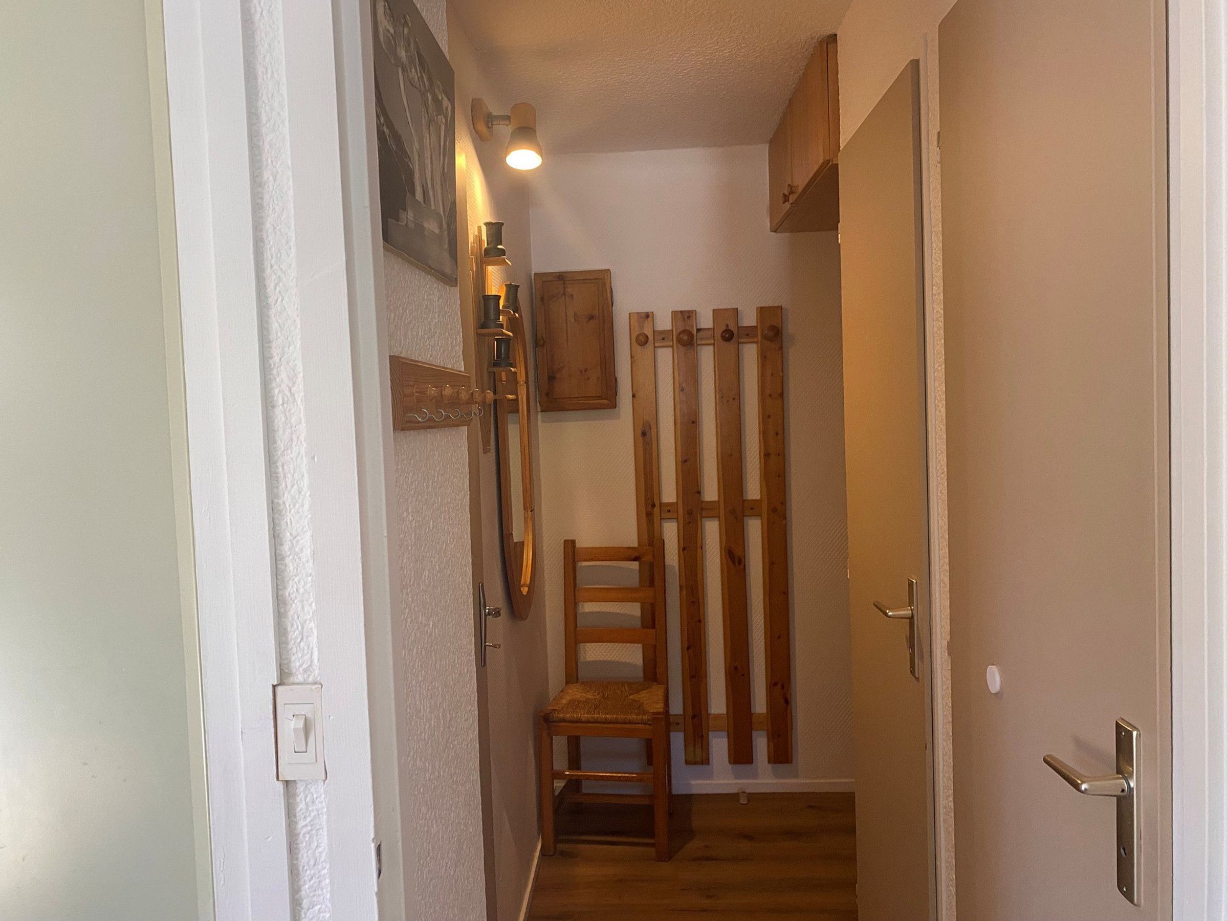 Un couloir étroit avec une chaise en bois, un porte-manteau et une porte dotée d’une poignée en métal.