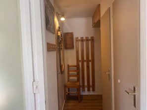 A narrow hallway with a wooden chair, a coat rack, and a door with a metal handle.
