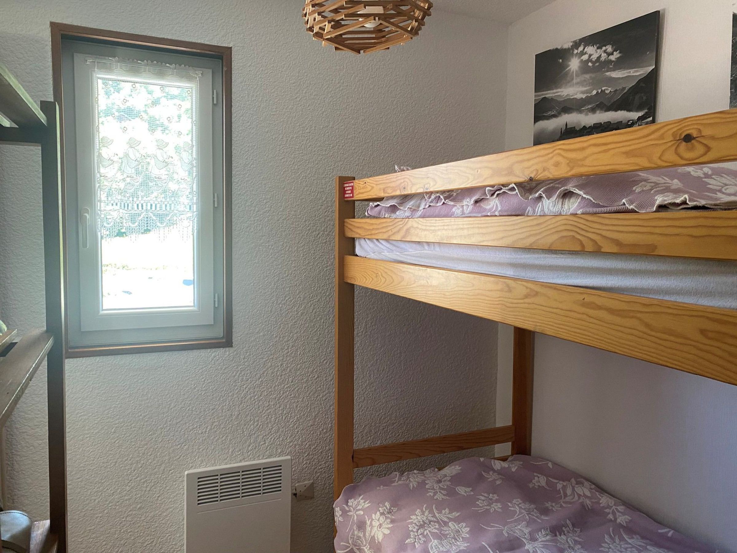 A bunk bed with a window, a radiator, and a wall-mounted picture.