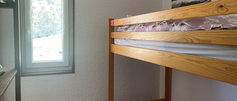 Un lit superposé avec une fenêtre, un radiateur et un tableau accroché au mur.
