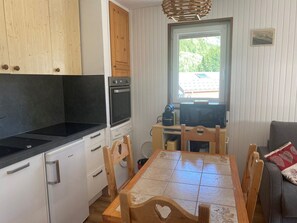 A compact kitchen with a stove, oven, and microwave. There is a dining table with chairs and a sofa in the living area.
