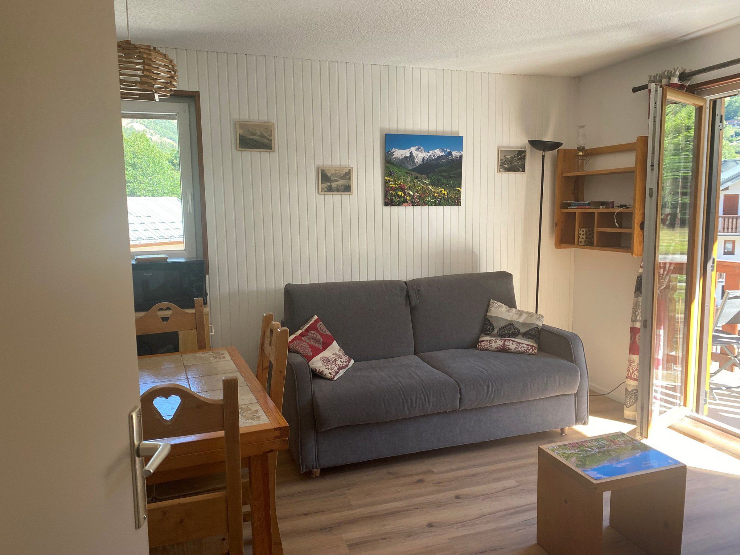 Un salón acogedor con un sofá gris, una mesa de comedor de madera y sillas. Hay cuadros en la pared y una ventana con vistas.