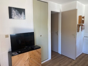 Una habitación con una televisión sobre un mueble de madera, una puerta con perchero y un cuadro colgado en la pared.