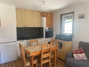 Eine kompakte Küche mit Holzschränken, einem eingebauten Ofen, einer Mikrowelle und einem Essbereich mit Holztisch und Stühlen.