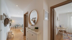 A modern hotel room with a wooden floor, a white dresser with drawers, a round mirror, and a small table with a laptop and chair. - Funchal Holidays, near the beach - Lido View Calla (Funchal)