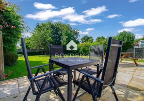 An outdoor patio with a table and chairs, surrounded by a garden and a wooden deck. - Located in one of the popular Frinton Avenues within walking distance of shops, cafes and beaches (Frinton-on-Sea)