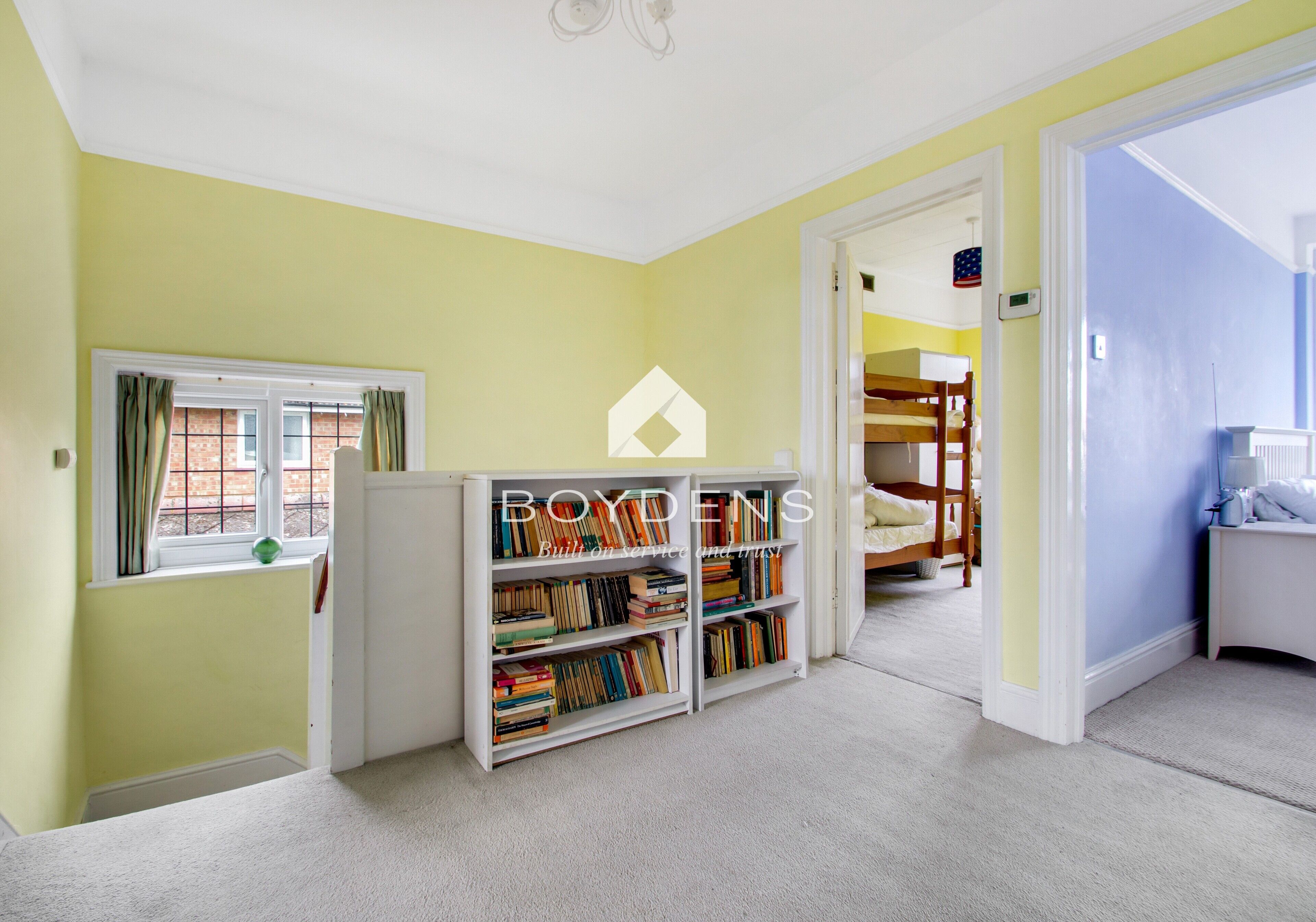 Une pièce avec une bibliothèque, une fenêtre avec des rideaux et, au fond, un lit superposé.