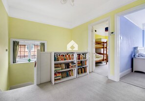 Een kamer met een boekenkast, een raam met gordijnen en een stapelbed op de achtergrond.