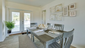 A dining area with a wooden table set for four, surrounded by chairs. There is a potted plant to the left and a door leading outside. - Airy Canal-Front Oasis in Cape Coral w/ Pool! (Cape Coral)