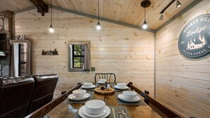 A wooden dining table set with white plates, silverware, and a centerpiece. The room features wooden walls, a stone fireplace, and a sign reading "Huskey Hill Lodge". - Pet Friendly! Hot Tub | Pool Table | Fire Pit (Pigeon Forge)