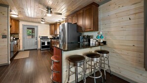 A modern kitchen with wooden cabinets, stainless steel appliances, and a bar area with stools. - Pet Friendly! Hot Tub | Pool Table | Fire Pit (Pigeon Forge)
